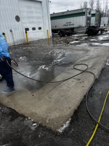 Blog 14 After: Pressure Washing A Soapy Concrete Pad With Water Draining Outside A Commercial Warehouse.